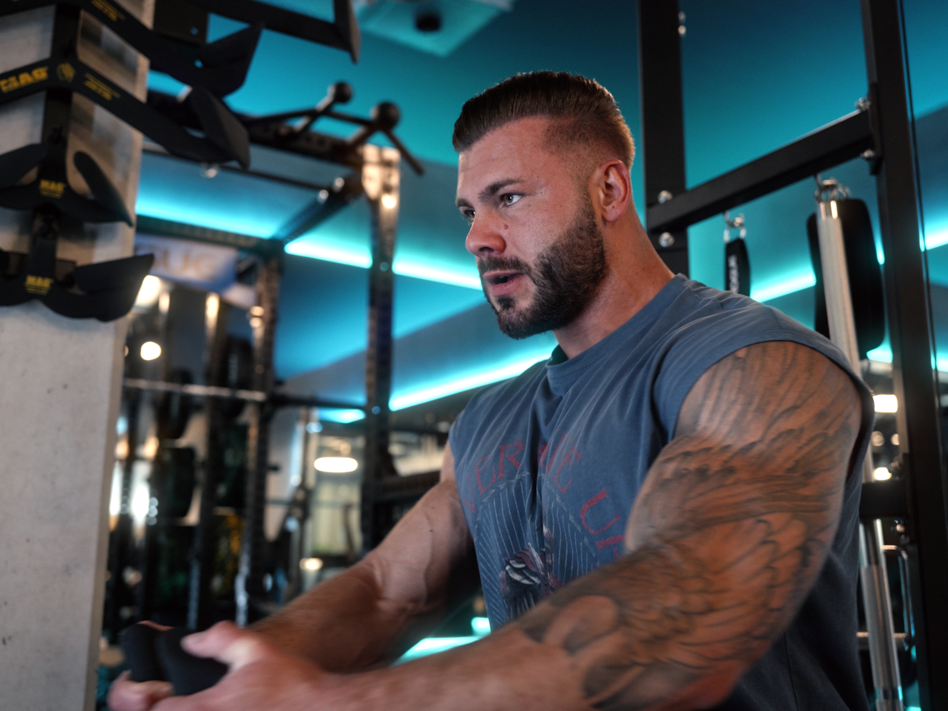 Muskelbepackter Mann mit Tattoo trainiert an einem Gerät im Fitnessstudio.