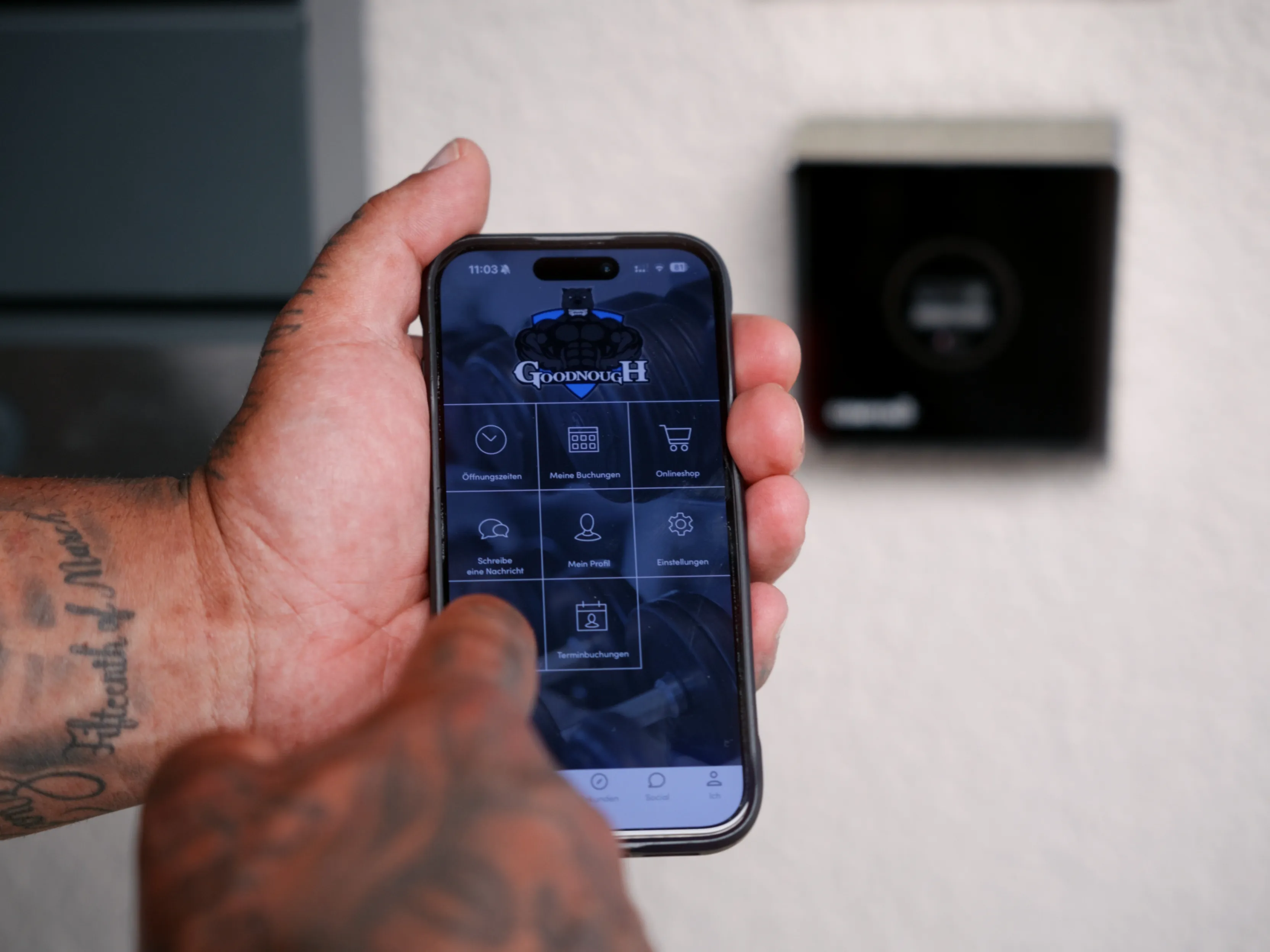Hand mit Tätowierungen hält ein Smartphone mit geöffneter Fitness-App GoodnoughH.