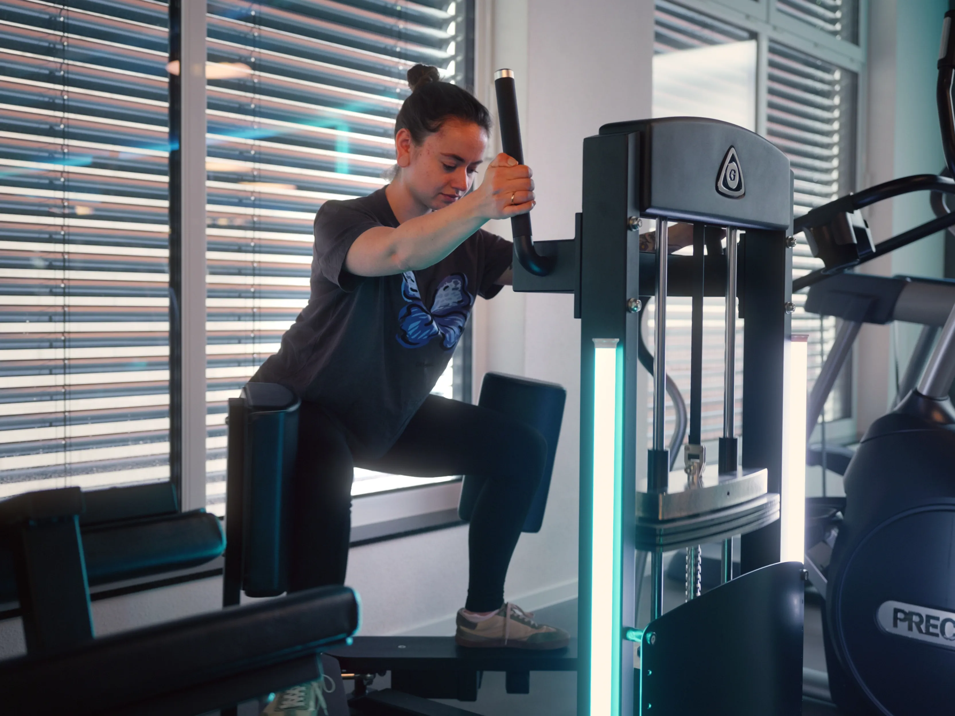 Frau trainiert an einem Fitnessgerät für die Beinmuskulatur im hellen Fitnessstudio.