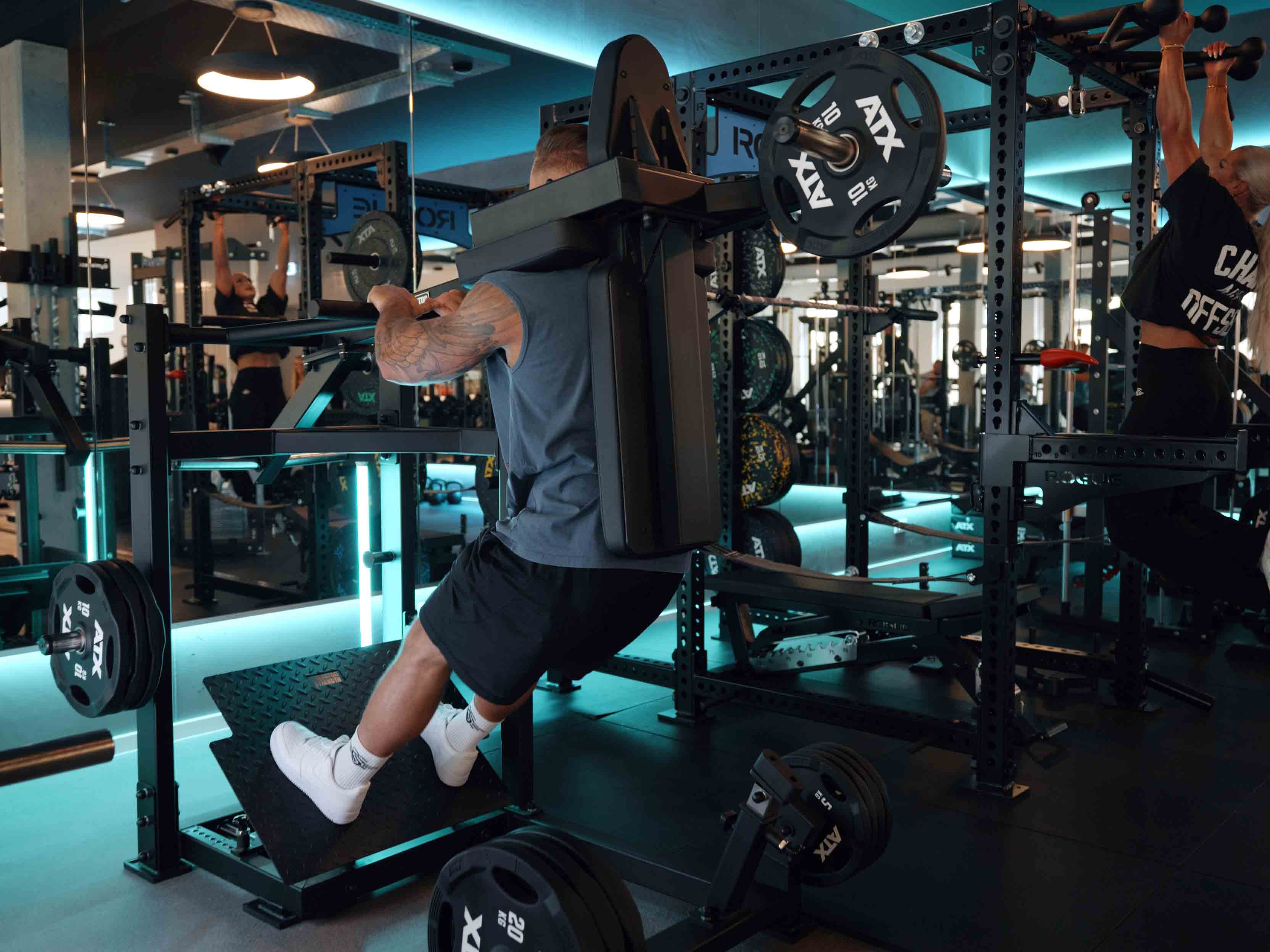 Mann trainiert Beine an einer Beinpresse im modernen Fitnessstudio mit Gewichten und Spiegeln.