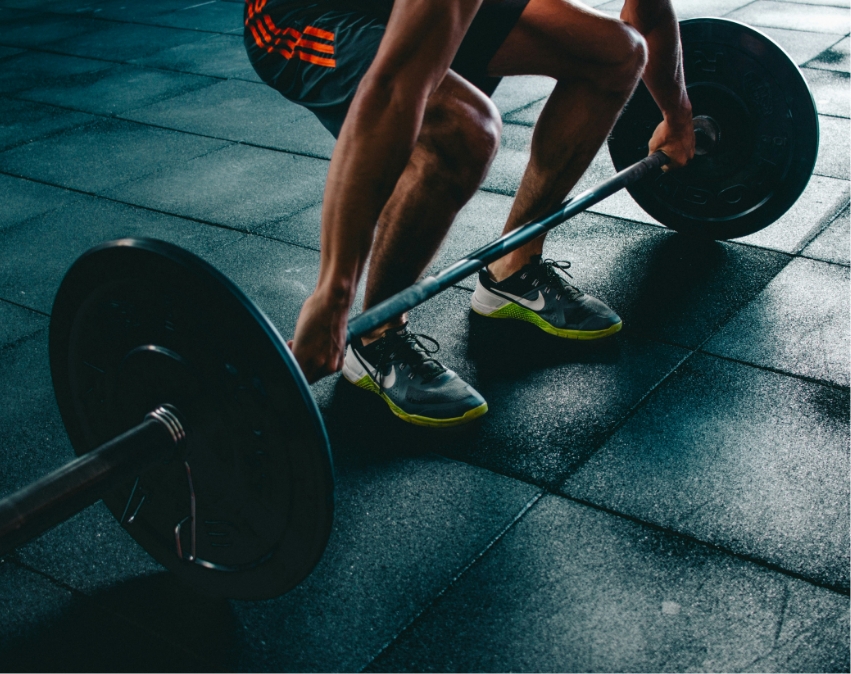Person hebt Langhantel mit Gewichten auf Gummimatten im Fitnessstudio.